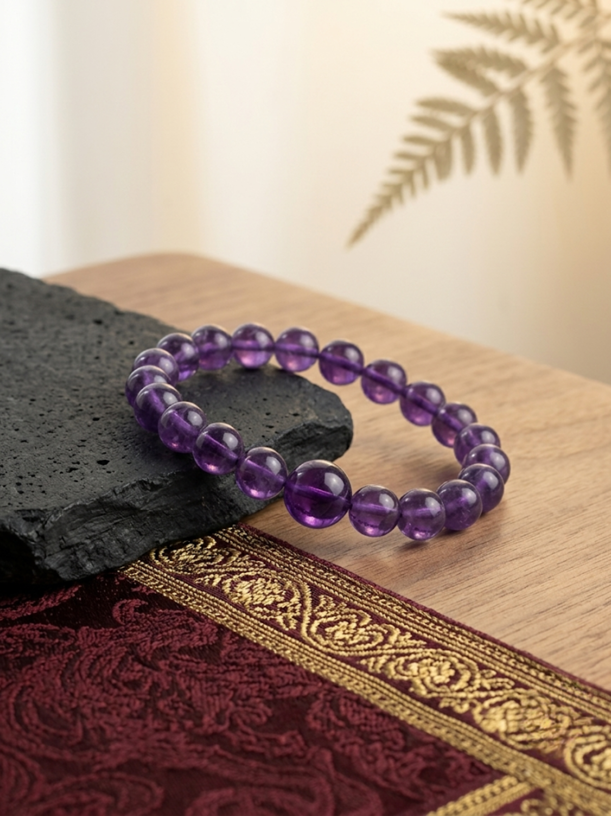 Angled lifestyle shot of the purple Amethyst 8mm beaded stretch bracelet resting on a textured black stone against a warm, neutral background.