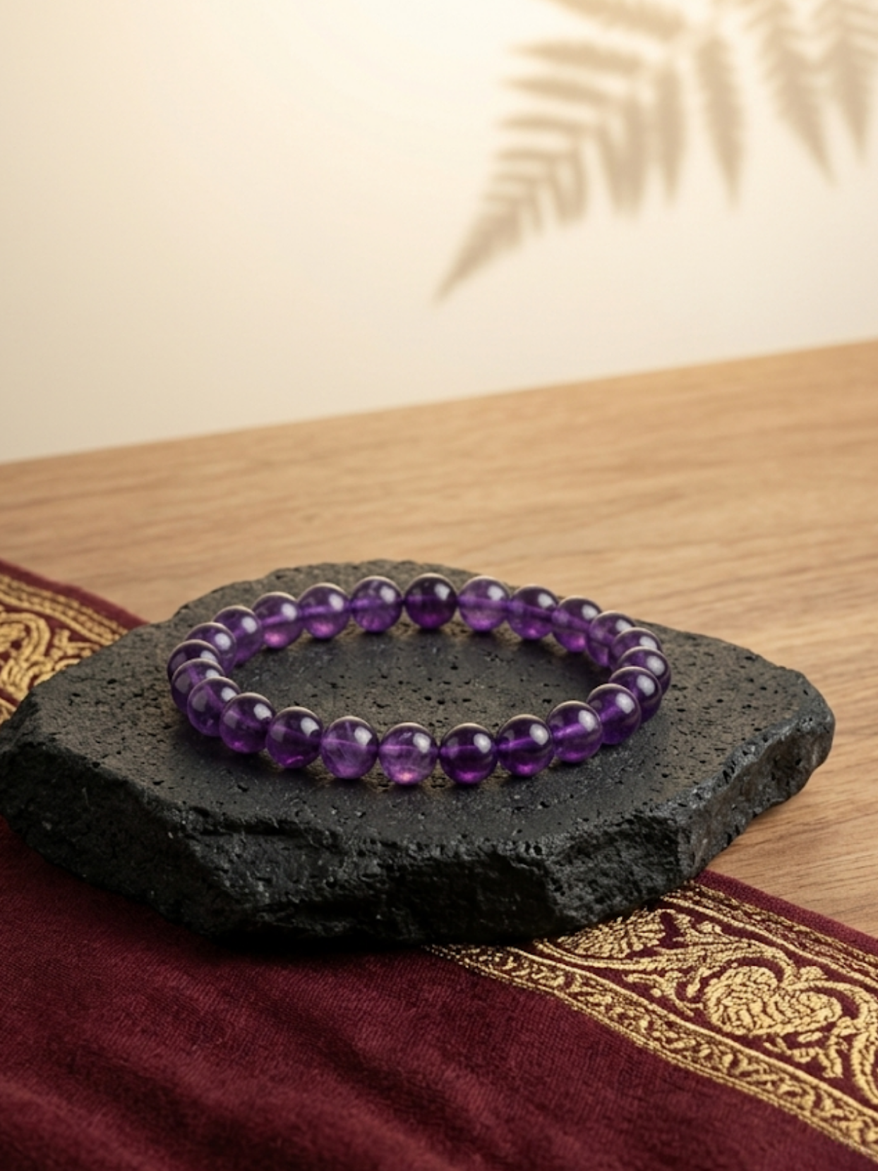 Front flat lay view of the Mani Monk Amethyst crystal bracelet alongside a raw Selenite plate, beautifully styled on a dark stone and traditional red cloth.