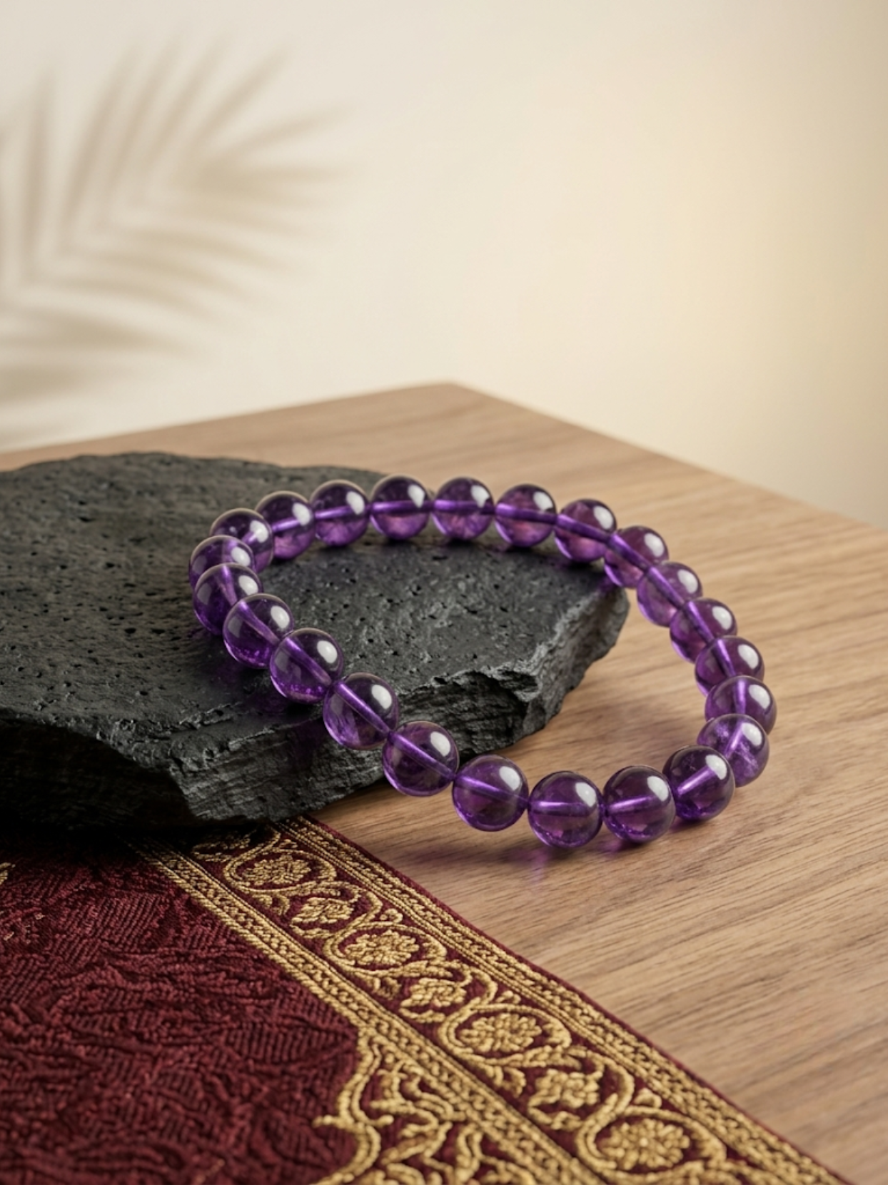 Angled lifestyle shot of the purple Amethyst beaded stretch bracelet paired with a raw Selenite charging plate, resting on a textured black stone against a warm, neutral background