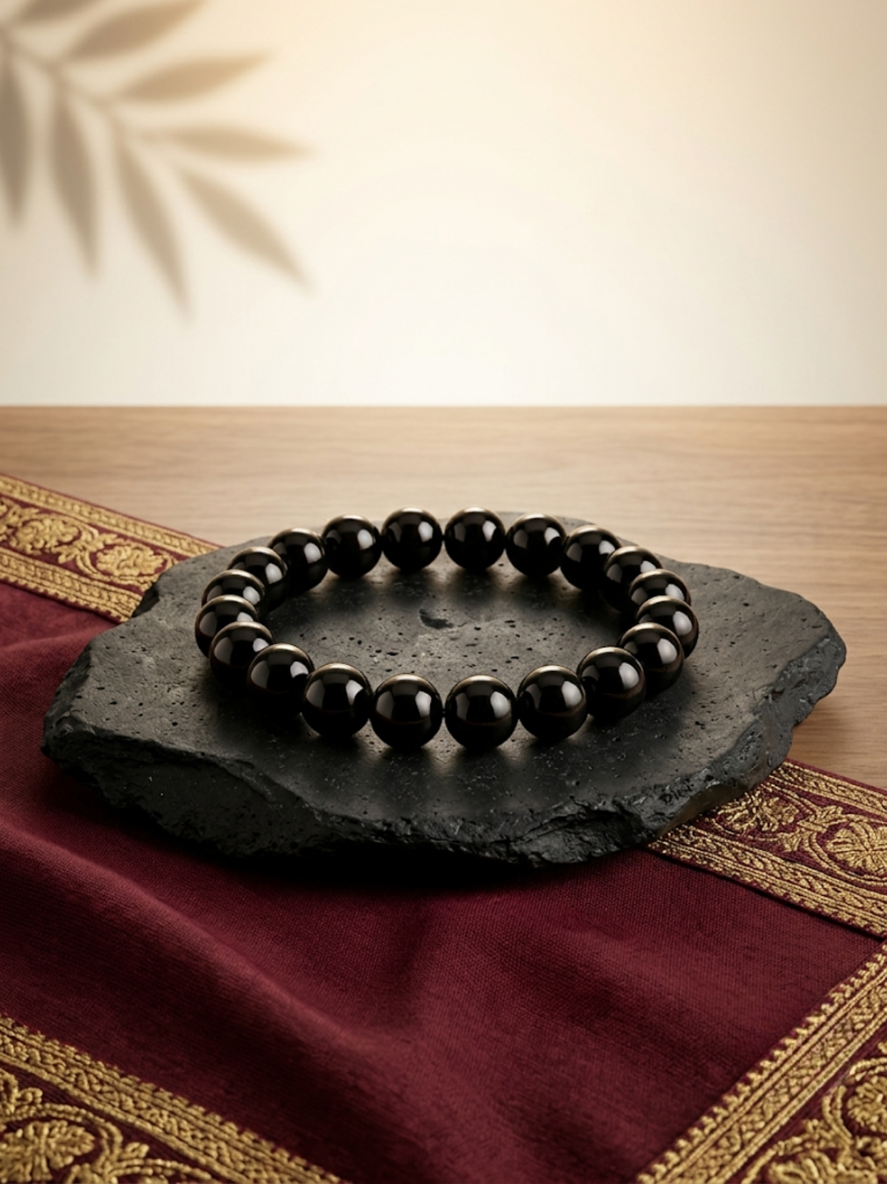 Front flat lay view of the Mani Monk Black Obsidian crystal bracelet, elegantly styled on a dark stone and traditional red cloth.