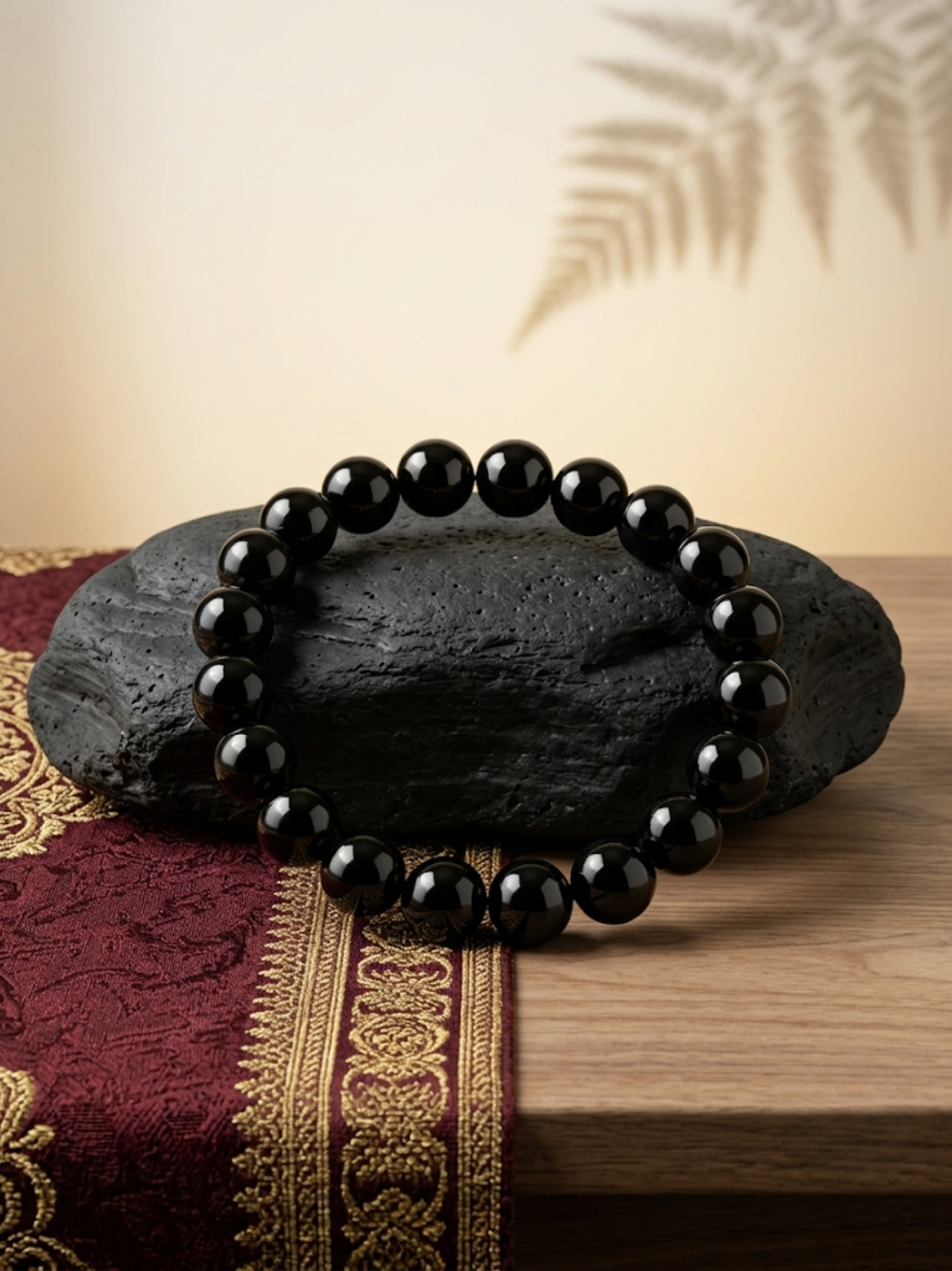 Angled lifestyle shot of the sleek Black Obsidian beaded stretch bracelet resting on a textured black stone against a warm, neutral background.