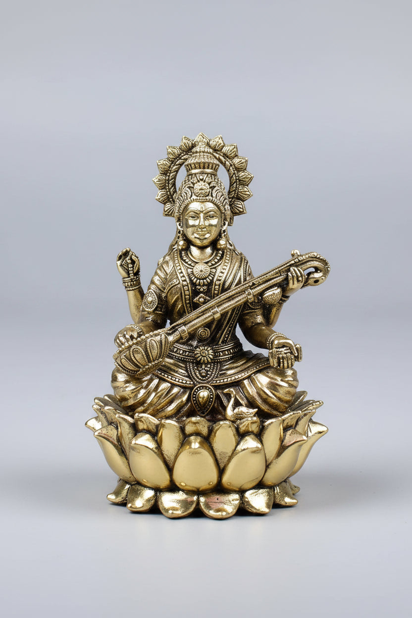 A brass statue of a seated deity playing a stringed instrument, mounted on a lotus base, photographed against a neutral gray studio background.