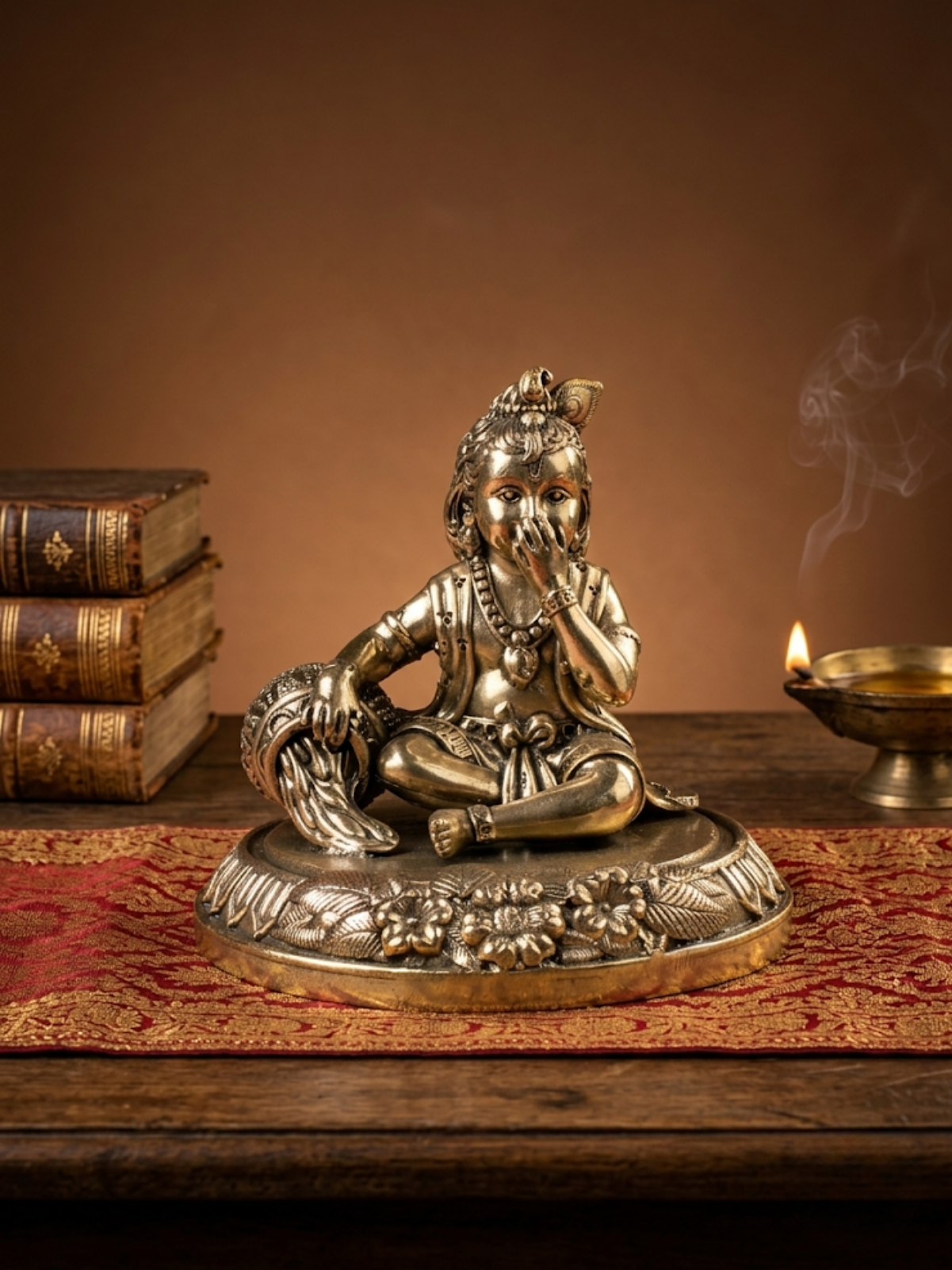 Front view of the Mani Monk Ashtadhatu Makhanchor Bal Krishna idol, styled on a traditional pooja altar with incense and a lit diya.