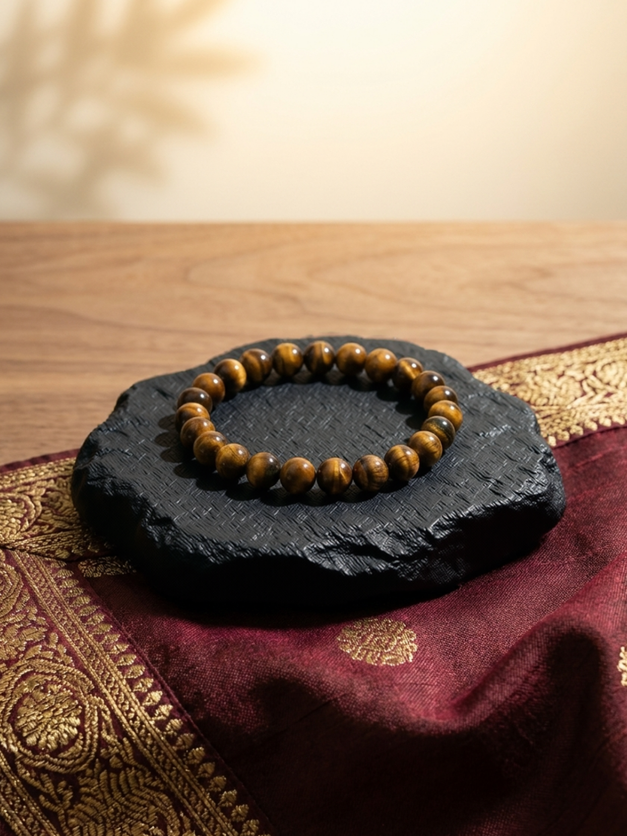 Front flat lay view of the Mani Monk Tiger Eye 'The Celeb' crystal bracelet, beautifully styled on a dark stone and traditional red cloth